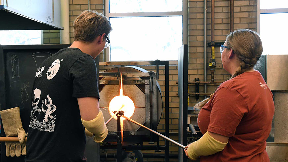 a boy and a girl working on ceramics in a lab-type setting