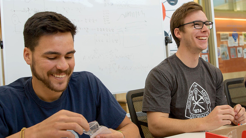 two design engineering students sitting at a table laughing and in conversation