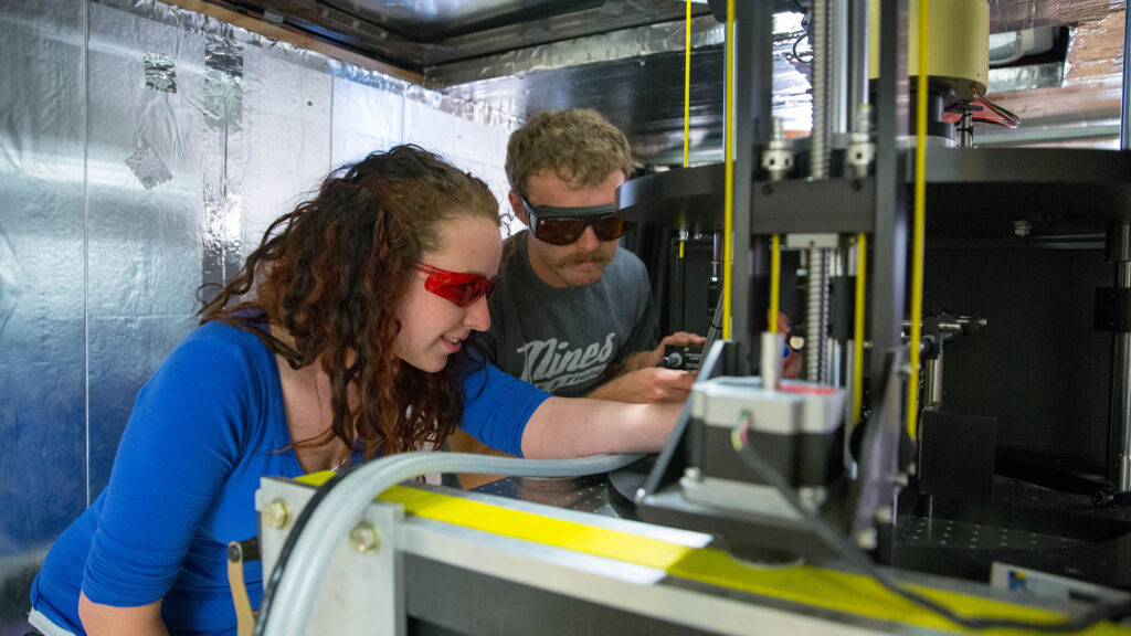 Two students focus on machinery in a lab