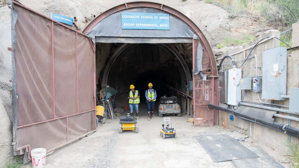 Students standing outside the Mines Edgar Experimental Mine controlling small droids in front of them.