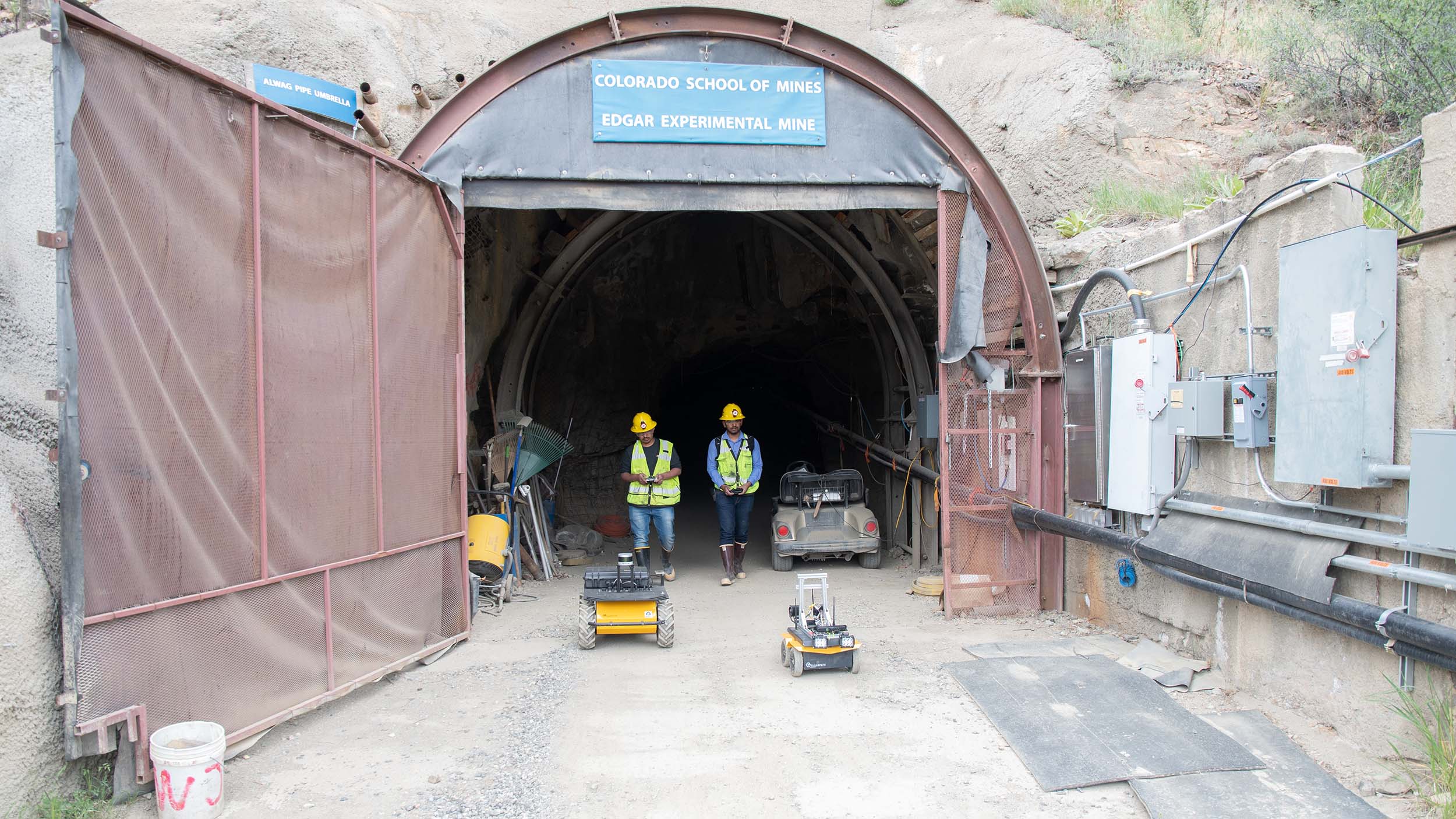 Mining Students standing outside the Mines Edgar Experimental Mine controlling small droids in front of them.