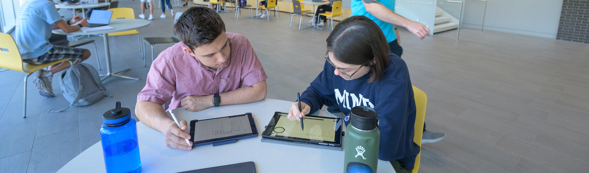 two students at table studying with laptop