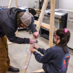 Two students working together on a large wooden frame