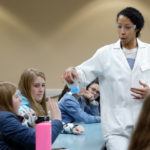 Female instructor of color showing an experiment to students