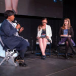 A black, female speaker on stage with two female students in a panel discussion