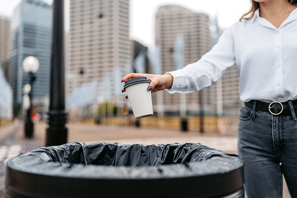Breaking up with paper coffee cup A woman throwing a paper coffee cup in a garbage can.