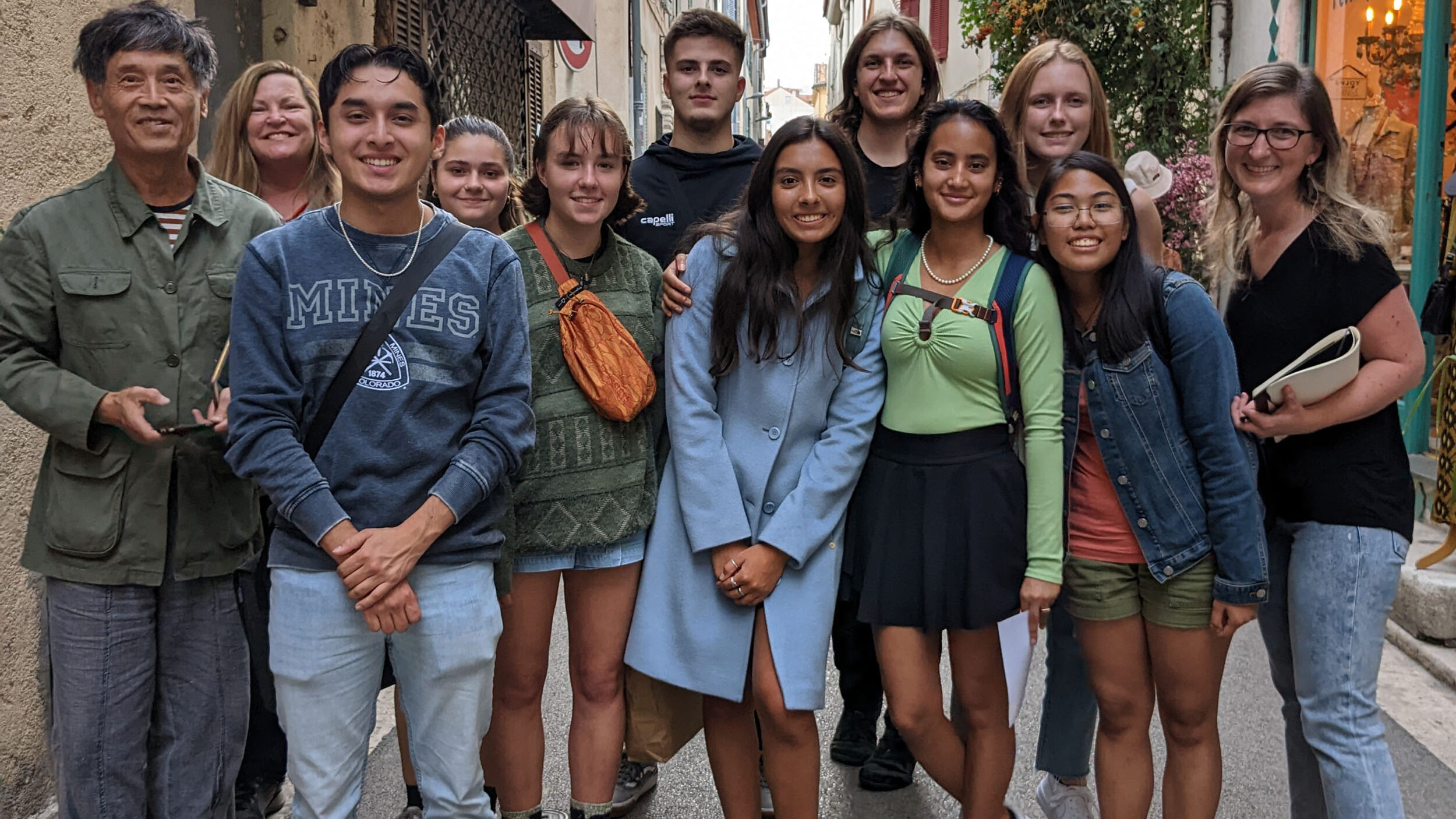 Group photo with college students, professors, and local artist, standing together on a narrow street in Antibes, France.