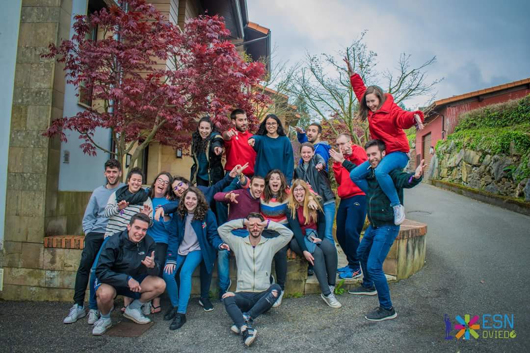 Students posing goofily in front of a building and a tree with fall colors