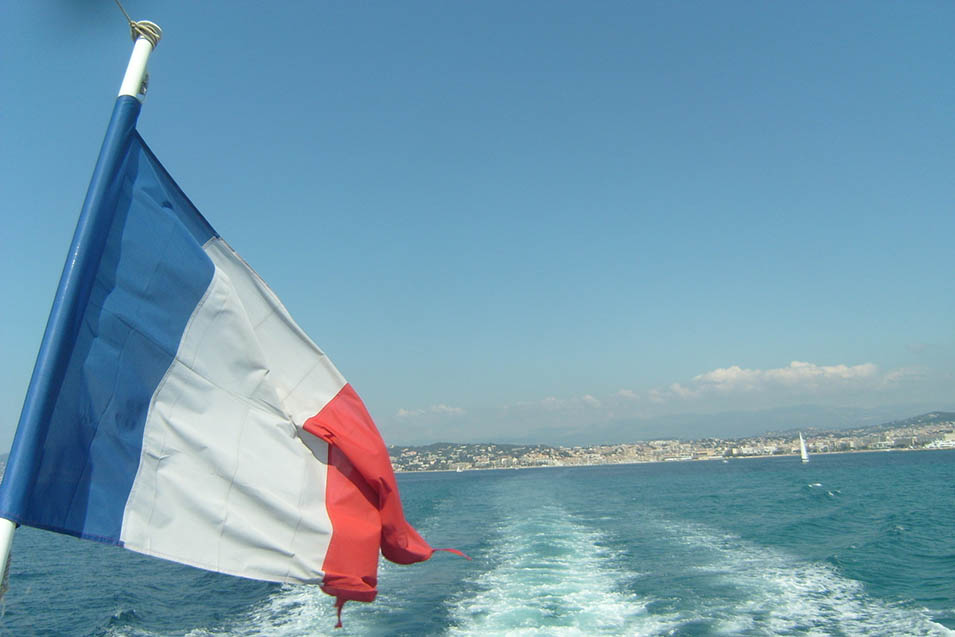 French flag on boat and wake of water from boat in background