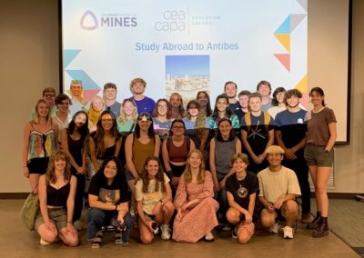 Group of over 20 students in front of a slide on a screen that says "study abroad to antibes"