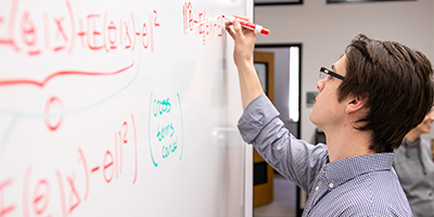 student working on math equation on whiteboard