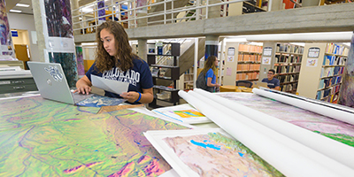 student sitting in library with maps covering table