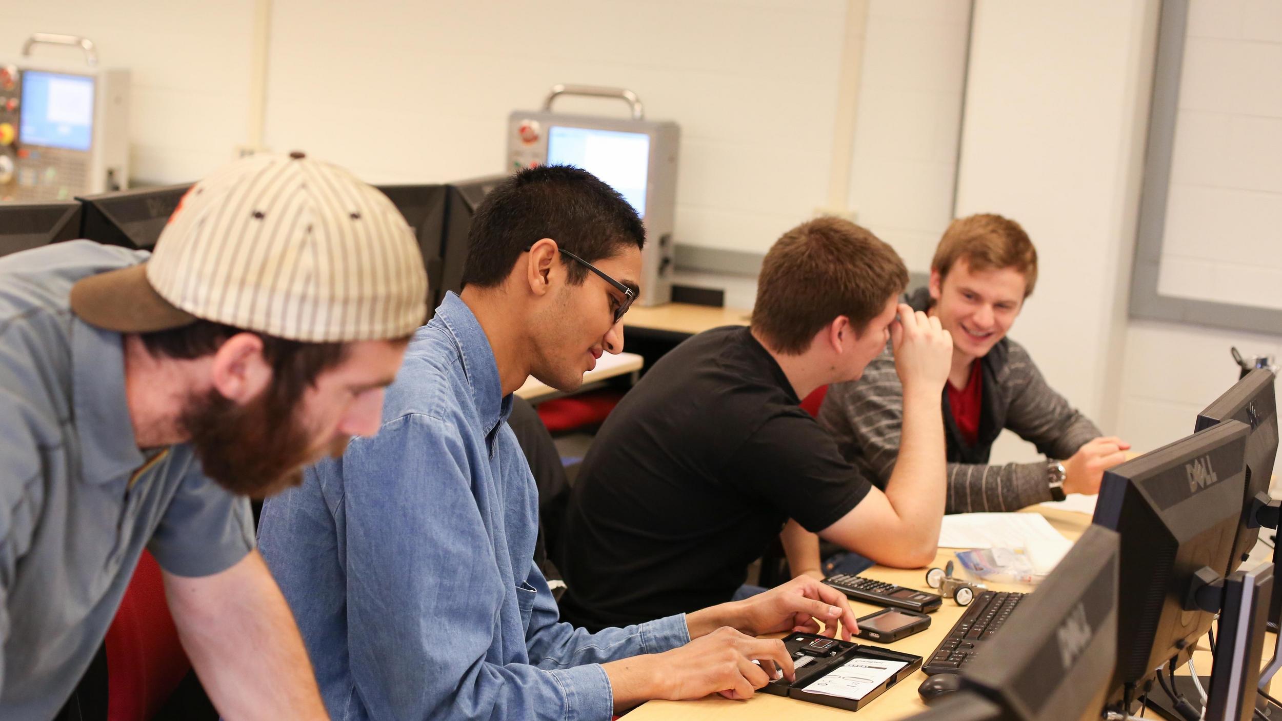 A group of men sitting around a computer in a classroom.
