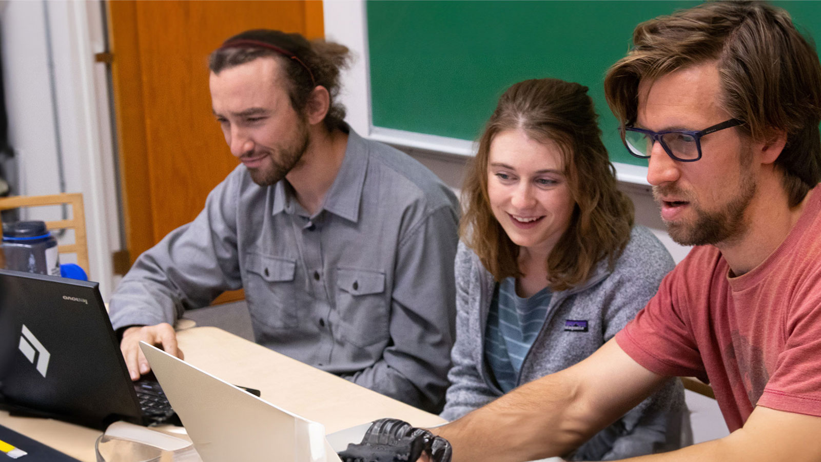 A group of people sitting around a table looking at a laptop.