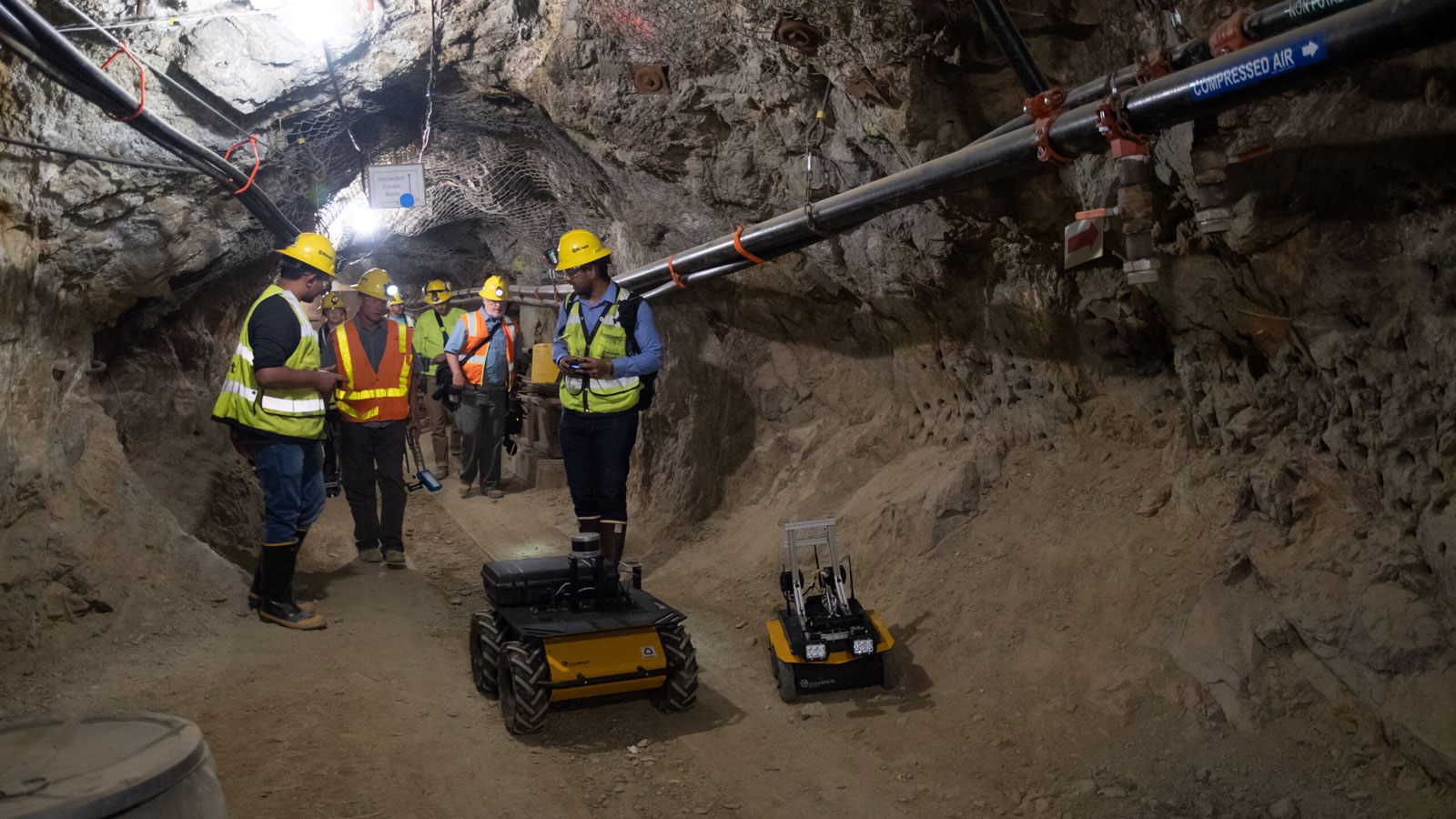 A group of men in hard hats and safety vests standing in a tunnel.