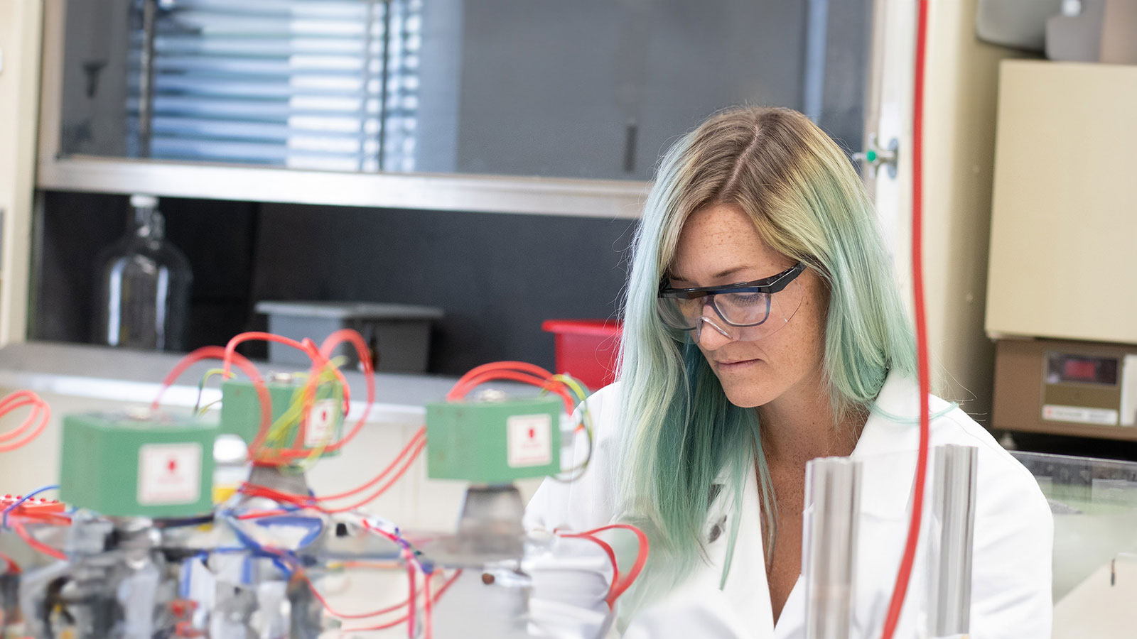 A woman in a lab coat and glasses working on a machine.