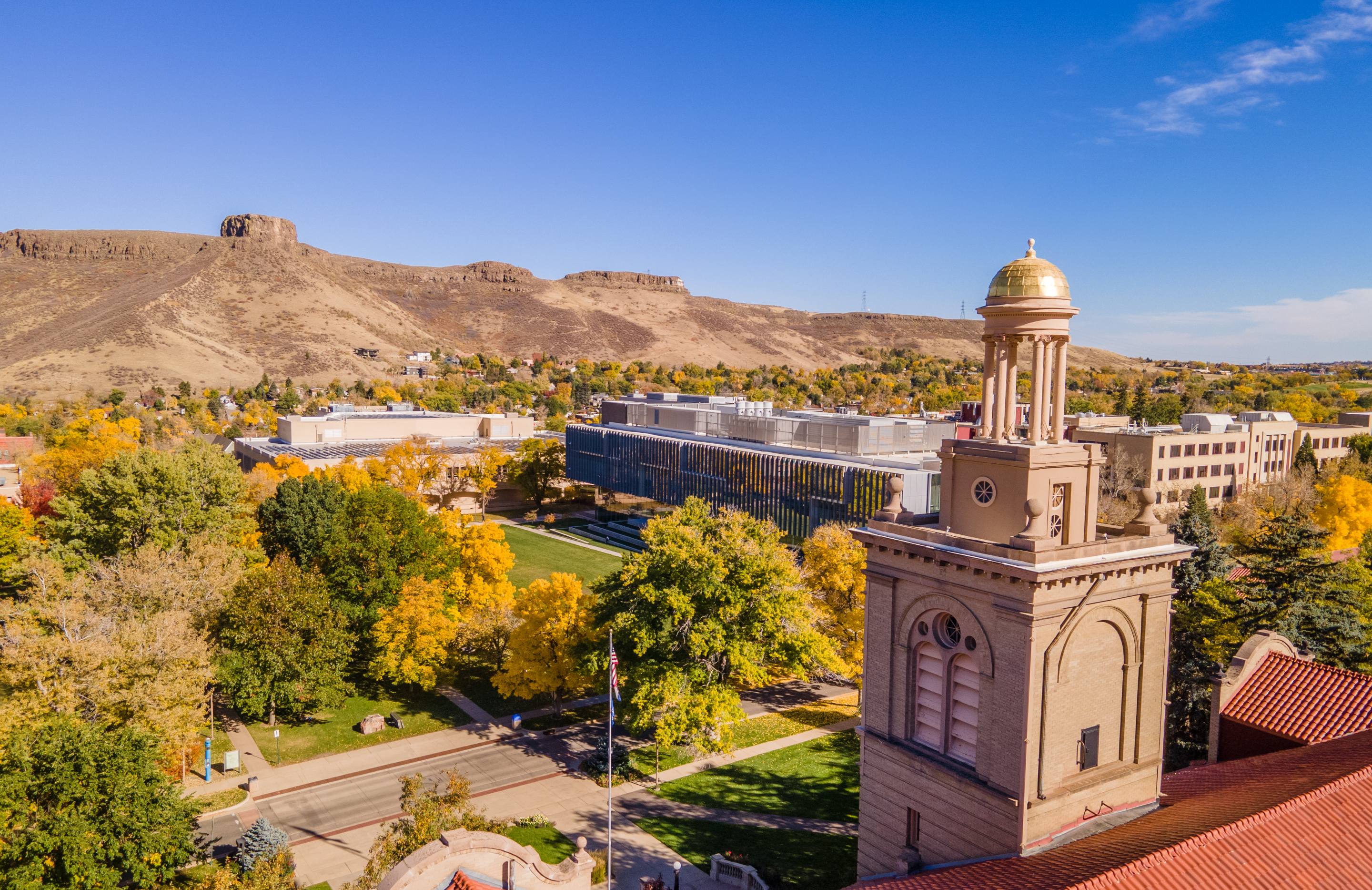 Aerial view from Guggenheim Hall's gold-domed tower overlooking campus buildings and fall foliage, with South Table Mountain in the distance.