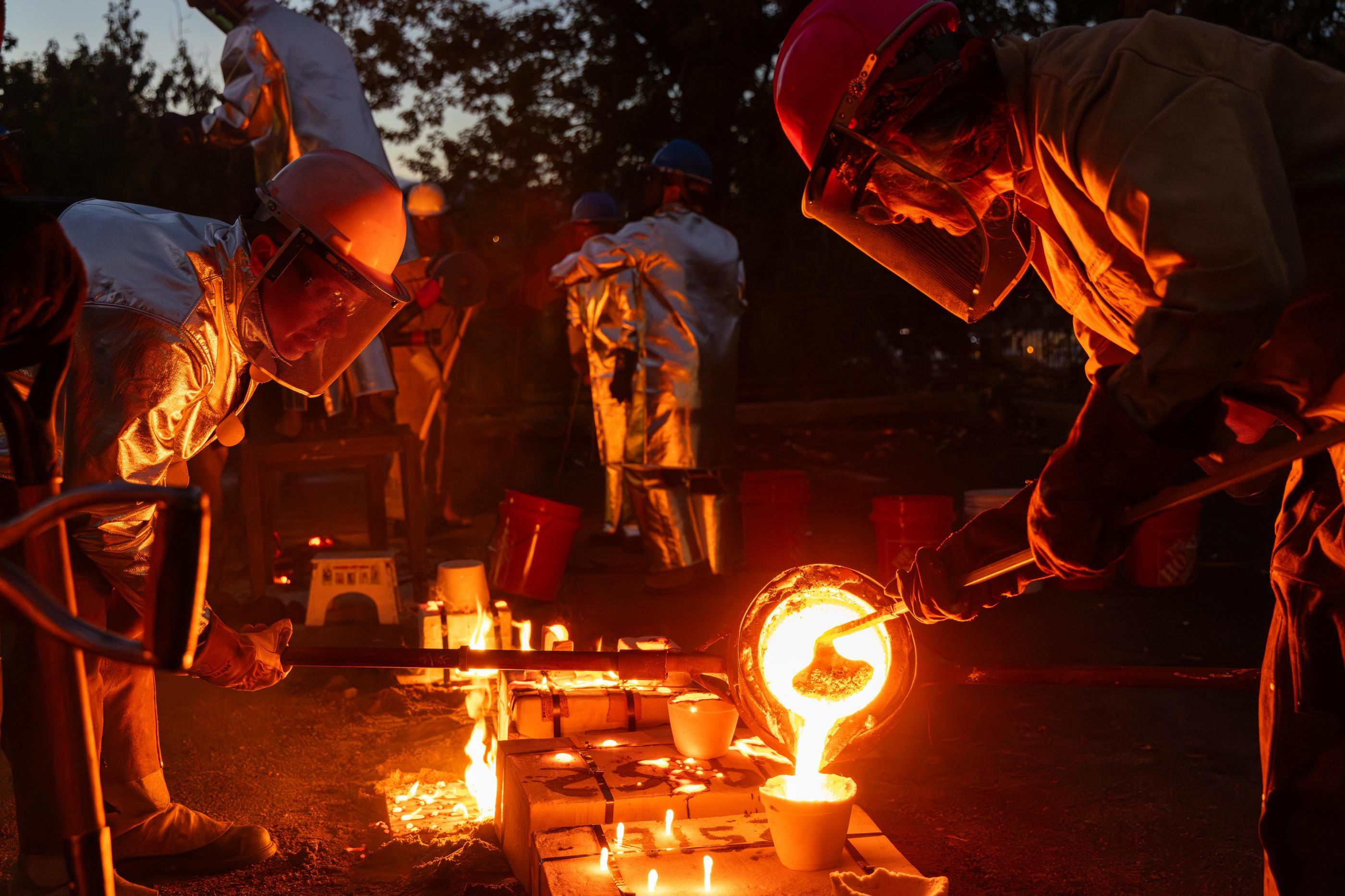 Students in protective gear pour molten iron into molds