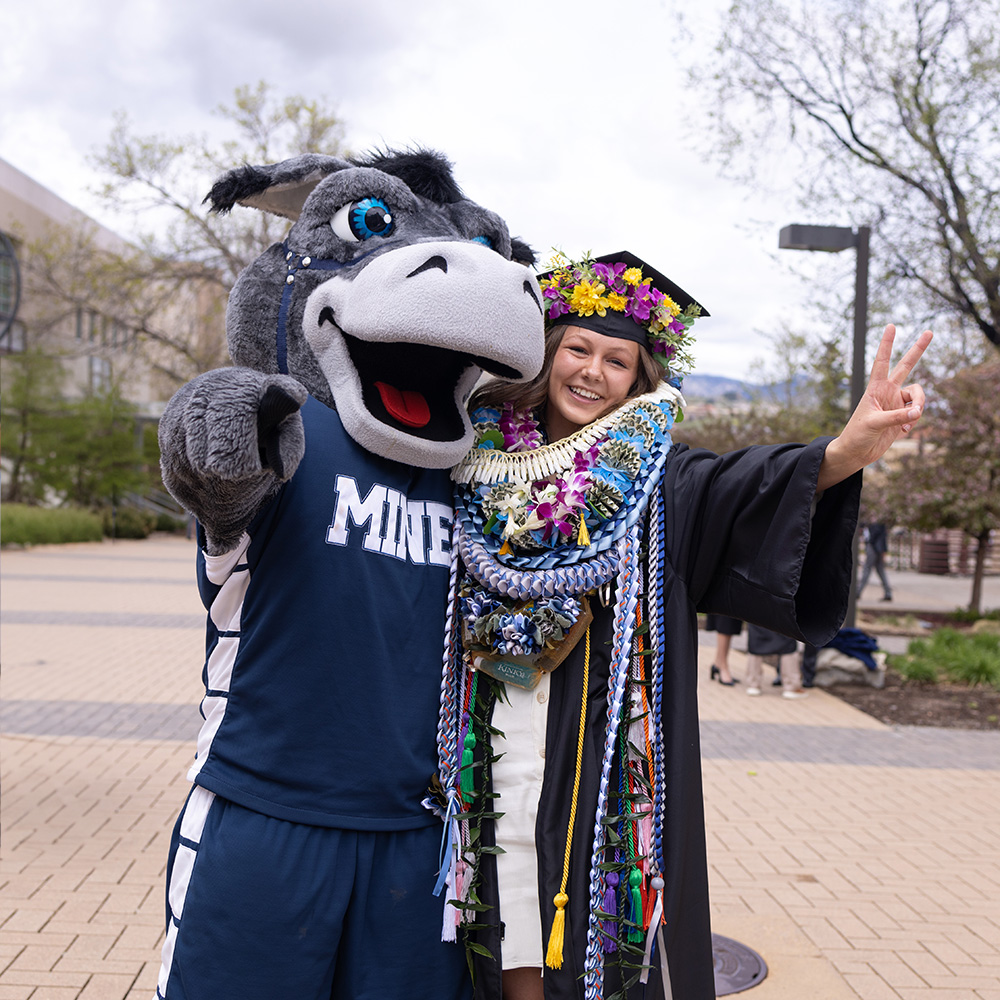 Blaster posing for a picture with a student graduating from Mines