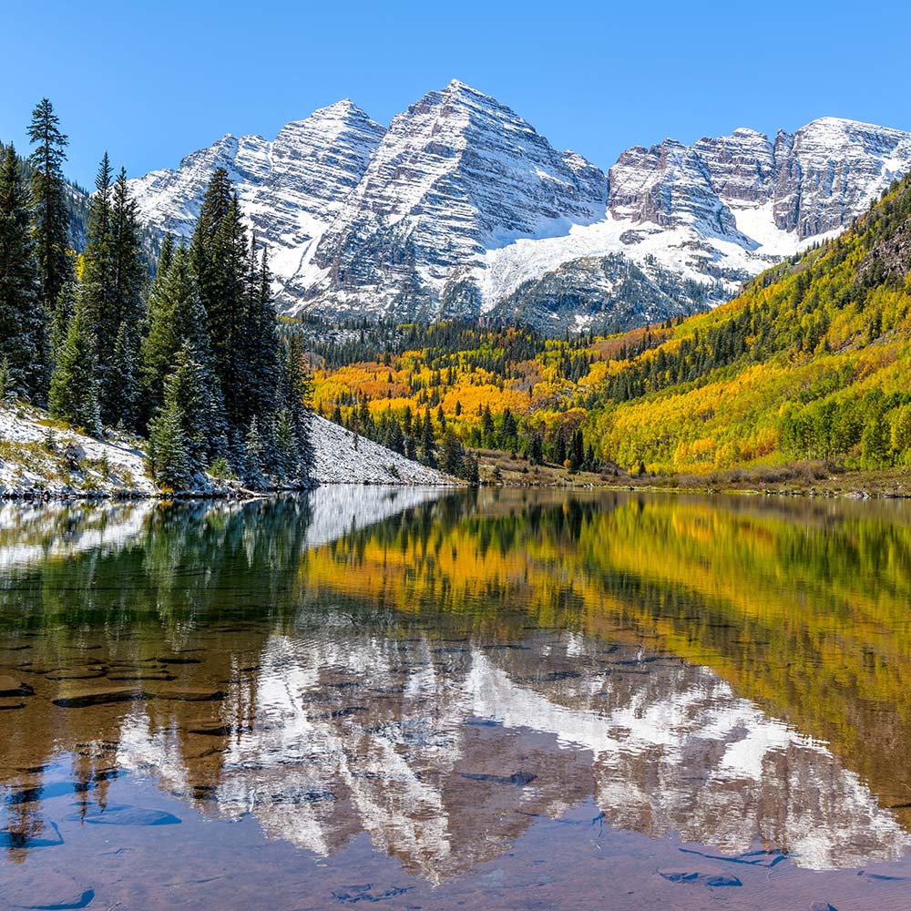 A wide-angle autumn midday view of snow coated Maroon Bells reflecting in crystal clear Maroon Lake, Aspen, Colorado.
