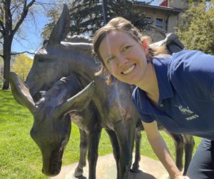 Picture of Emma Griffis standing next to the "A Friend to Lean On" sculpture at Mines of two burros.