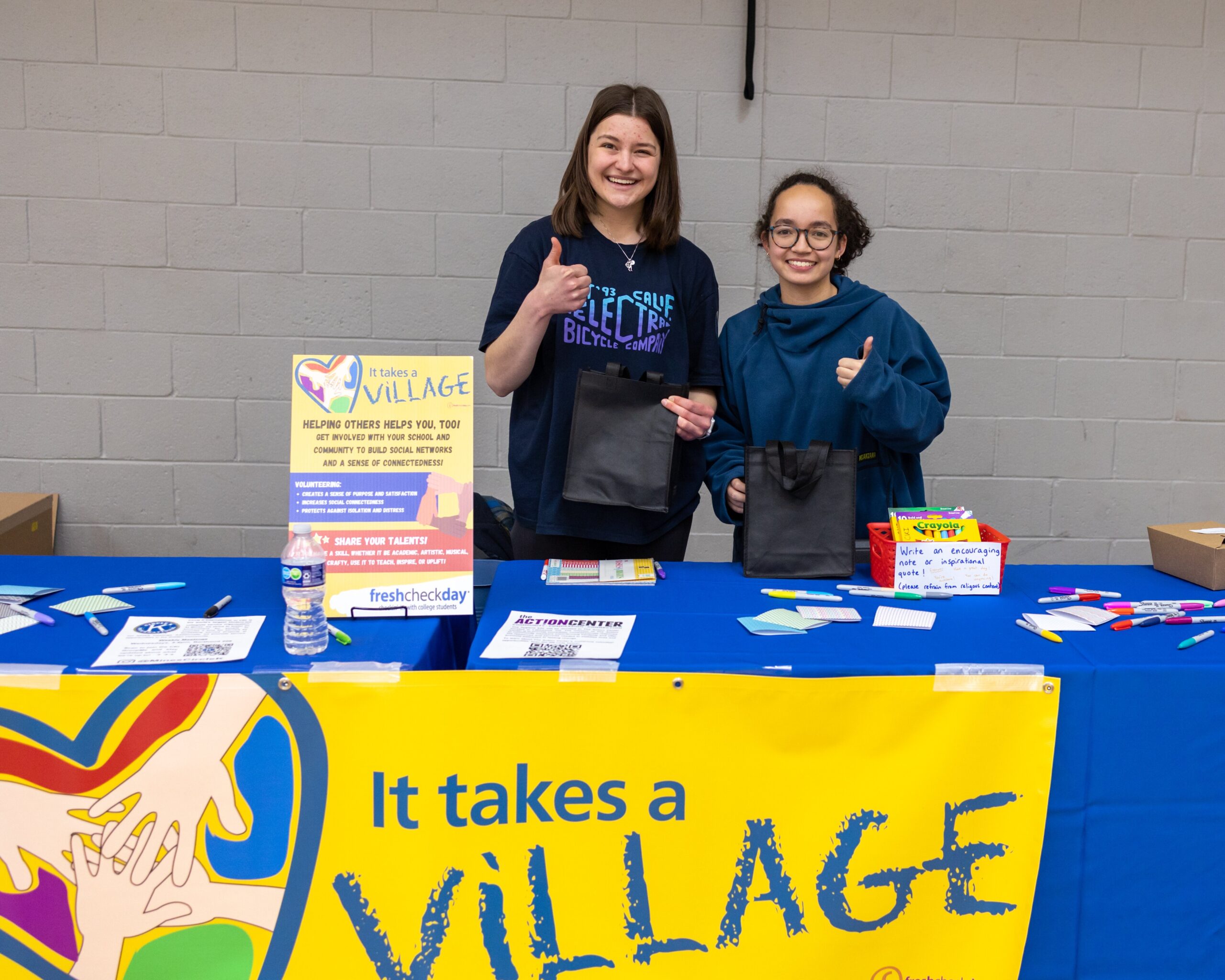 Two students have their thumbs up at the "It Takes a Village" booth.