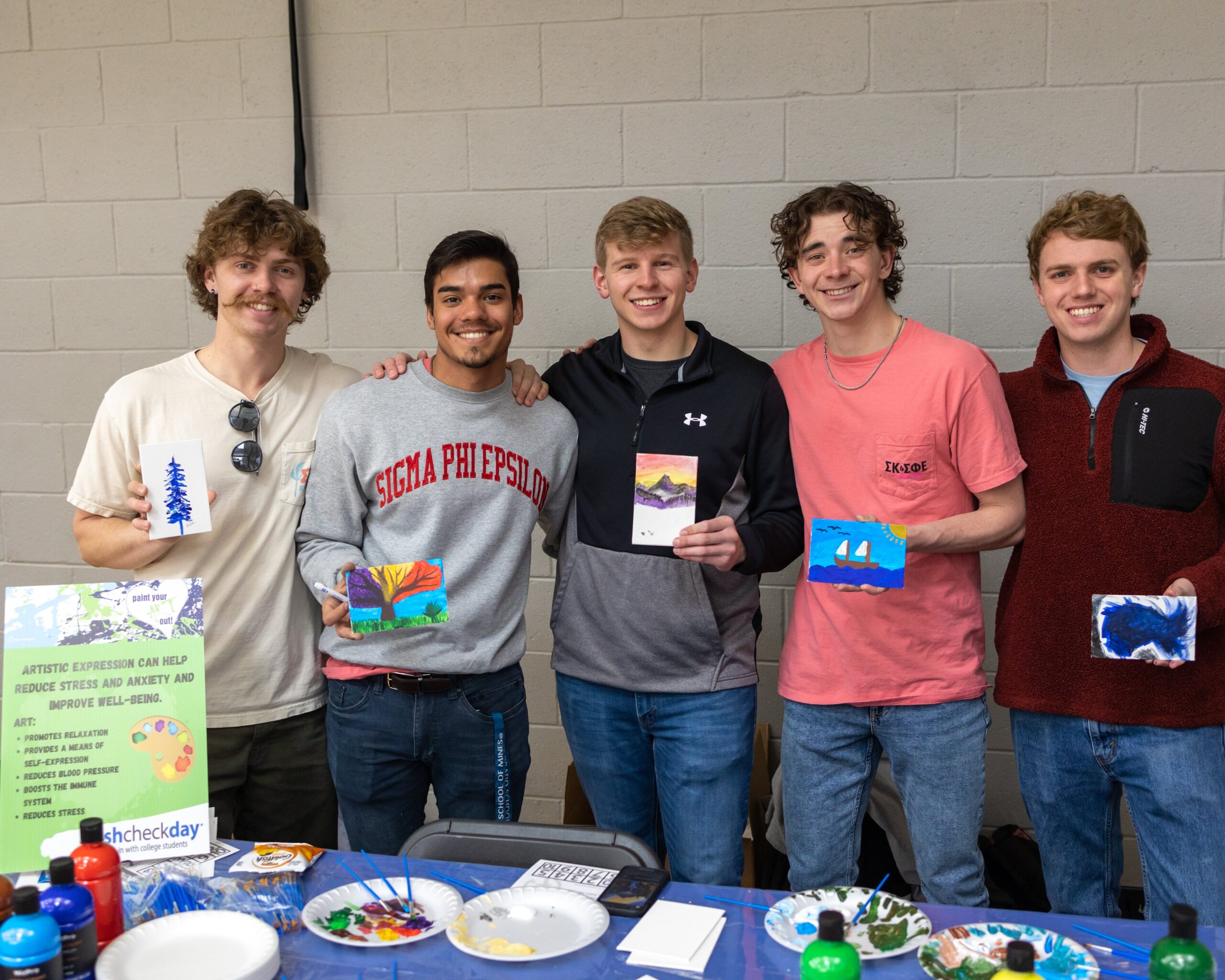 Students hold up small canvas paintings at the "Paint Your Art Out" booth.