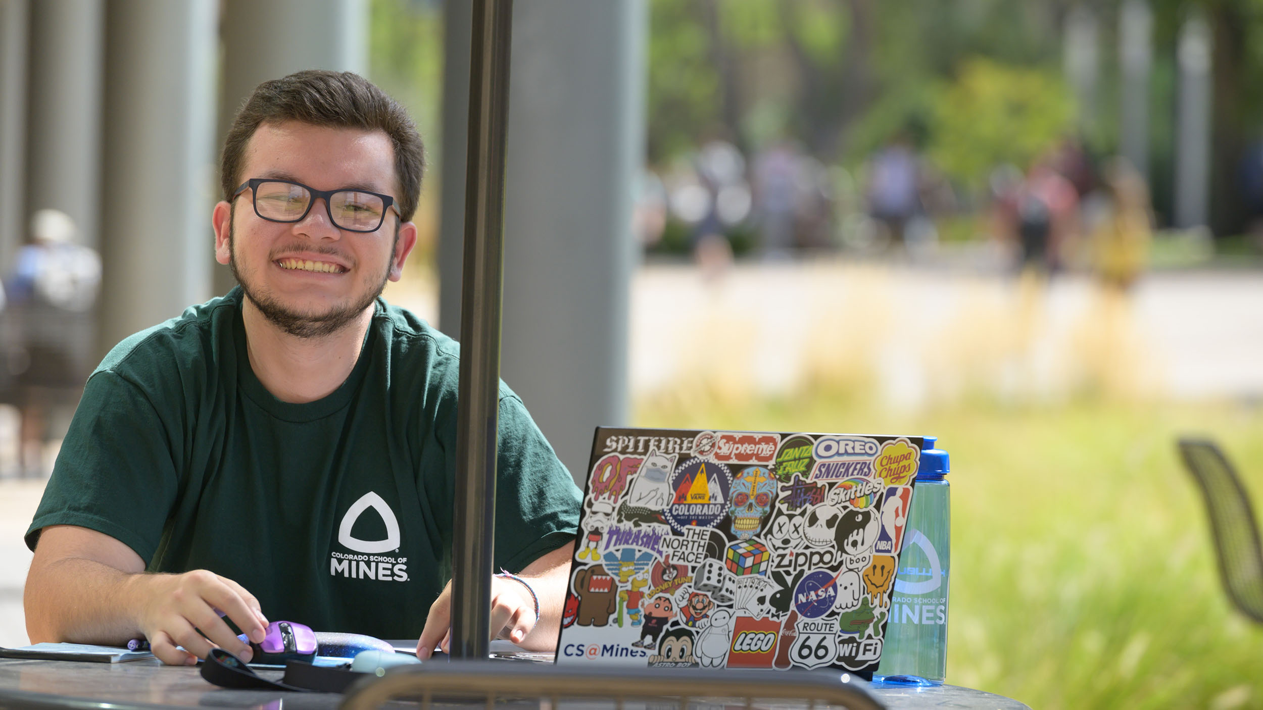 Student sitting at a table outside working on a laptop