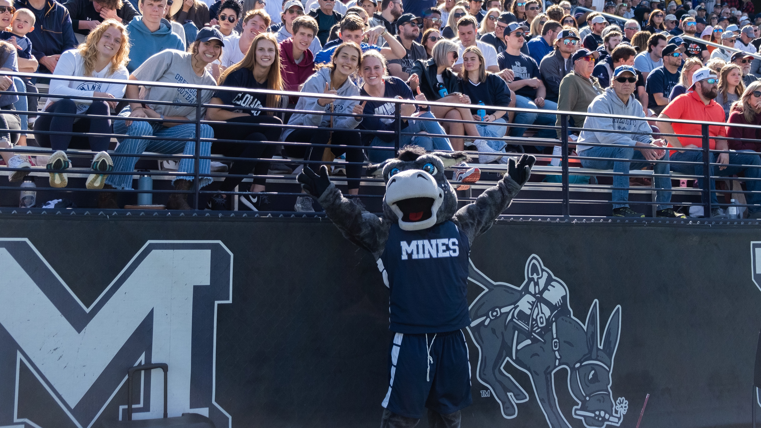 Blaster the Mascot posing with a crowd at a Mines homecoming football game