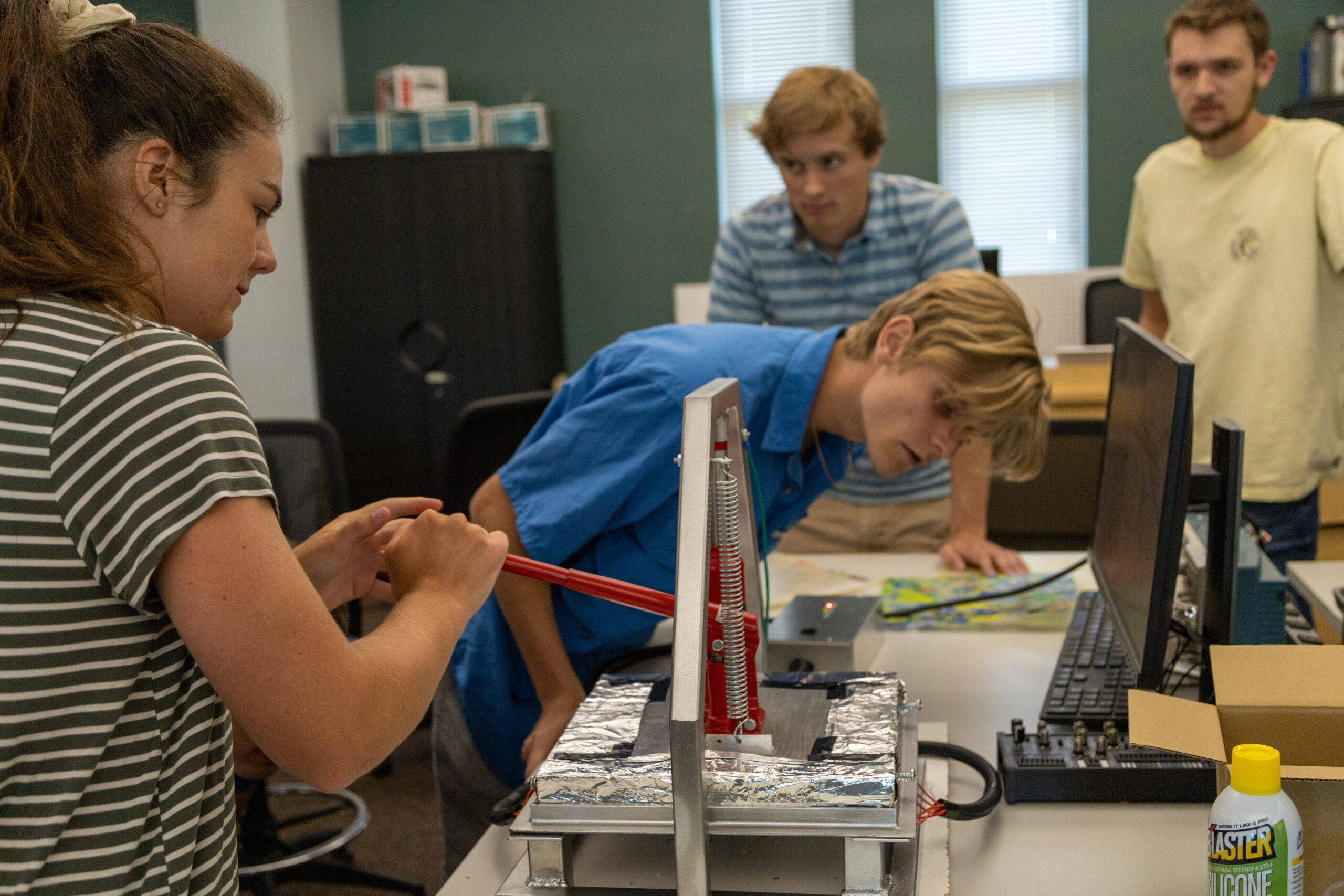 Student compressing a lever in a spring loaded device while other students look on