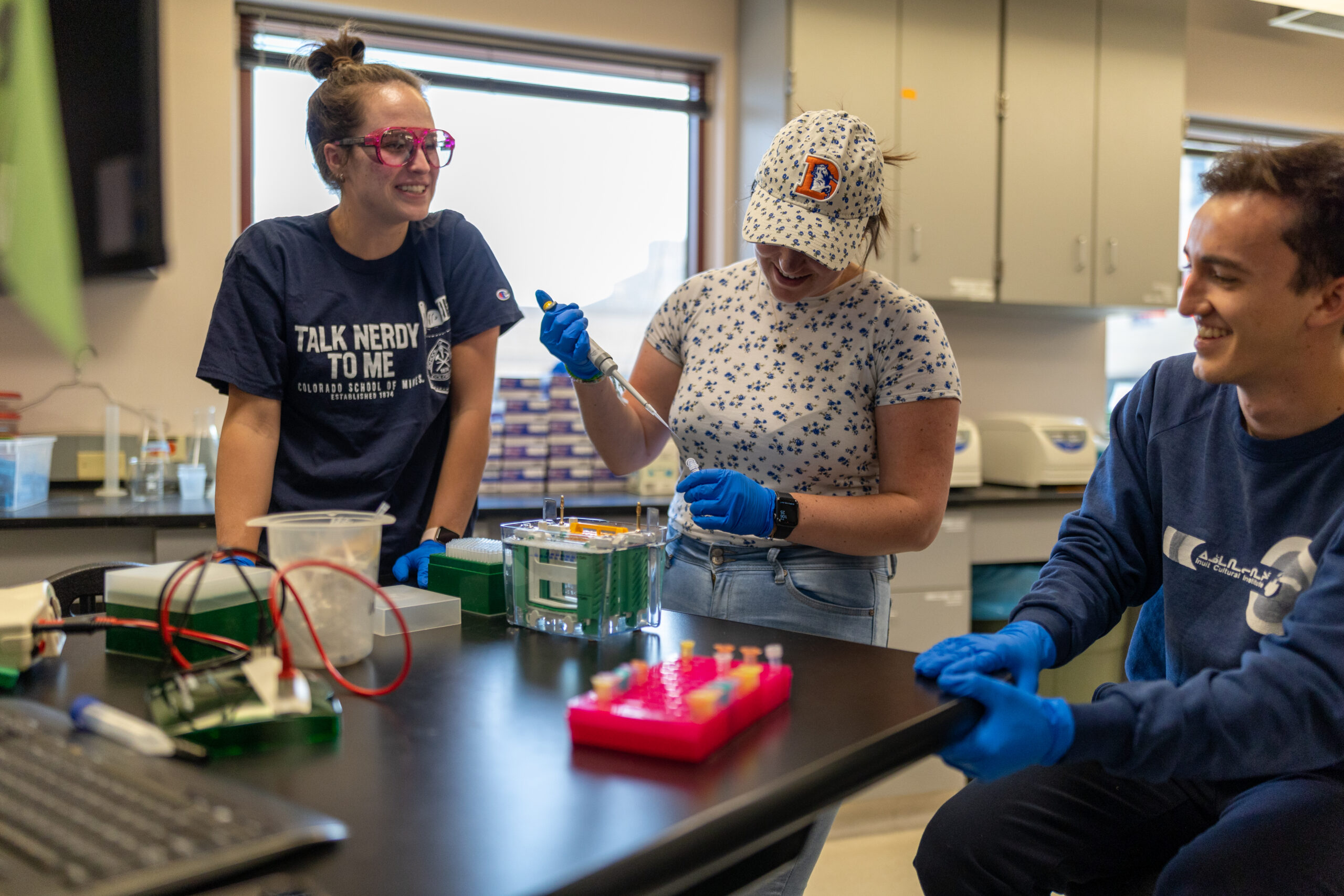 Three students a lab table with one using a pipette to transfer something from a test tube.