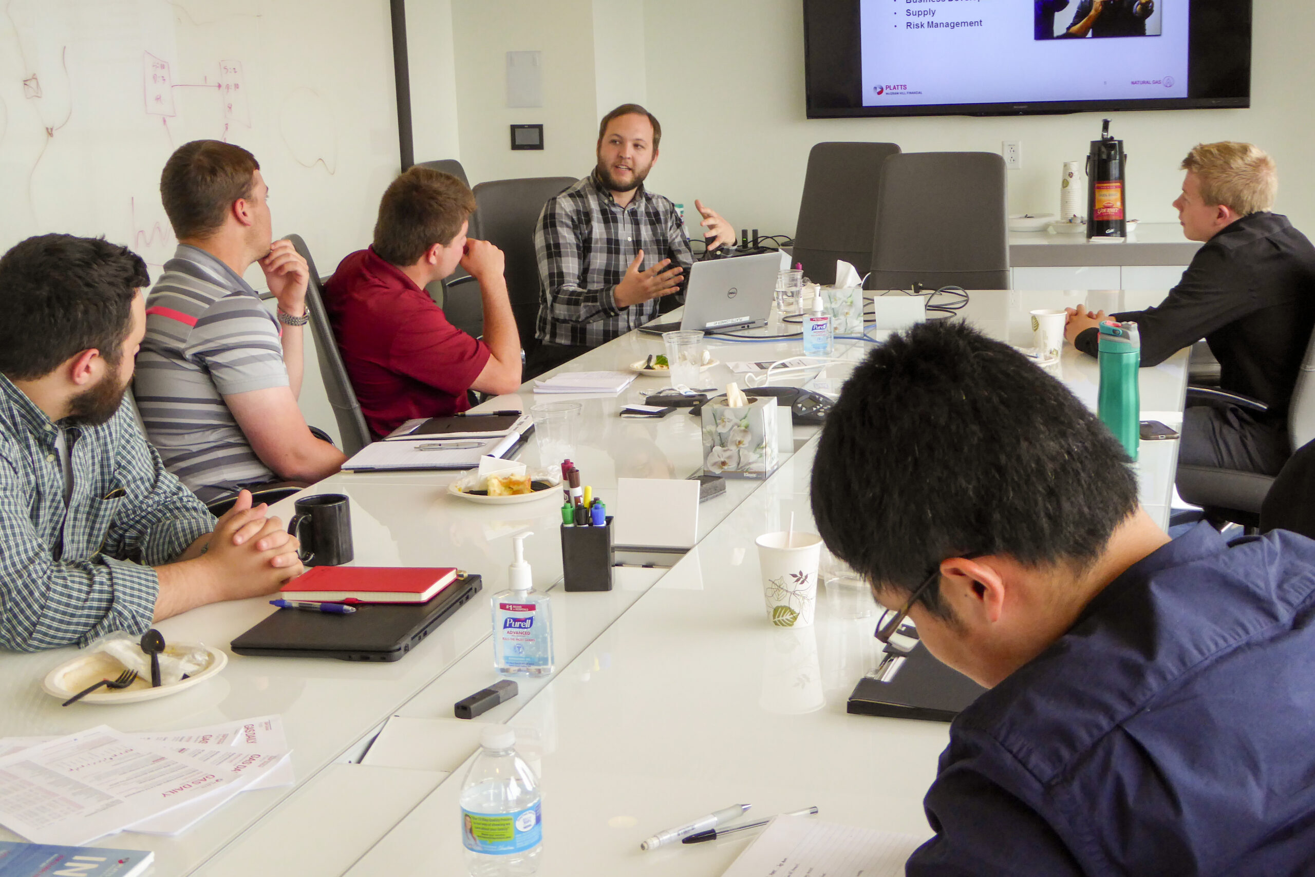 Students around a table listening to a professor explain a slideshow about a business.