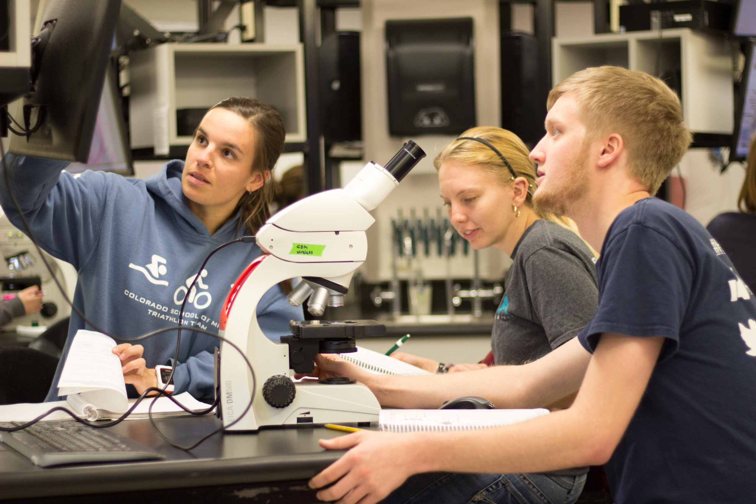 Students around a microscope looking at a display screen. 