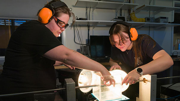Two mechanical engineering graduate students with earphones on working with equipment in a lab 