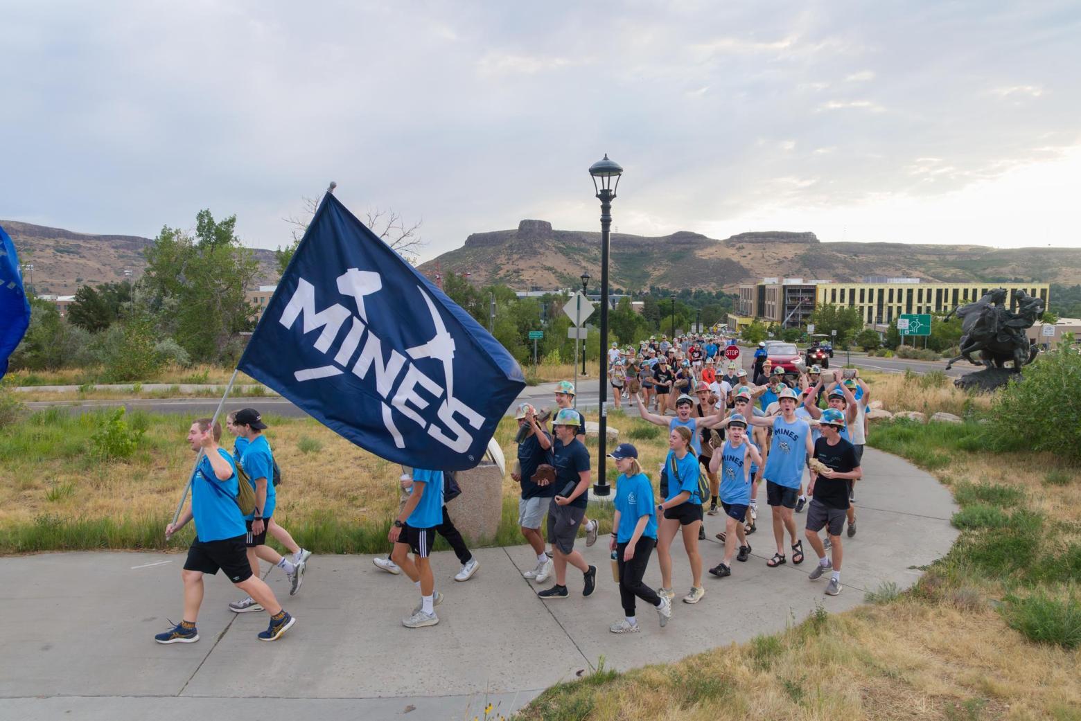 Mines incoming students starting the M Climb holding a Mines flag and celebrating their start at Mines
