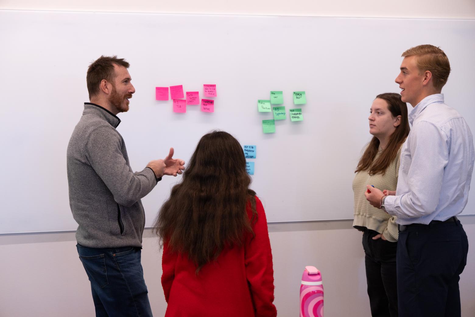 Engineering and Technology Management Engineering and technology management students and professor discuss at a whiteboard, surrounded by colorful sticky notes, while engaging in a brainstorming session